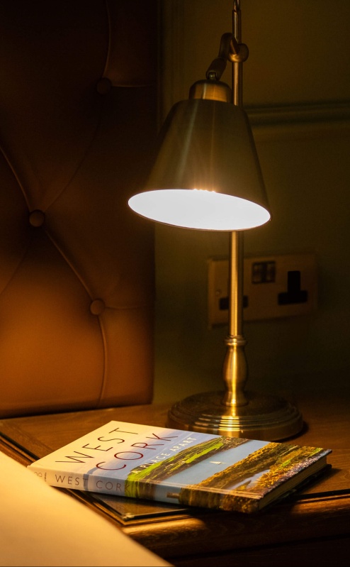 Cosy hotel room with a lamp and books on a bedside table.