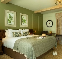 Elegant hotel room with a luxurious bed, open doors to a sunny patio garden.