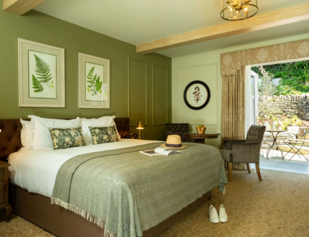 Elegant hotel room with a luxurious bed, open doors to a sunny patio garden.