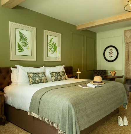 Elegant hotel room with a luxurious bed, open doors to a sunny patio garden.