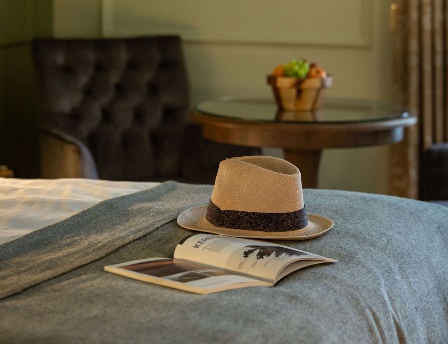 Elegant hotel room with hat and book on bed, art on wall, and seating area.
