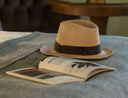 Elegant hotel room with decor, a cosy chair, and a hat on a bed.