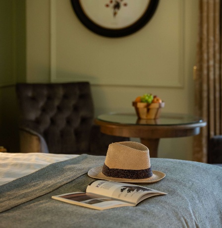 Elegant hotel room with hat and book on bed, art on wall, and seating area.