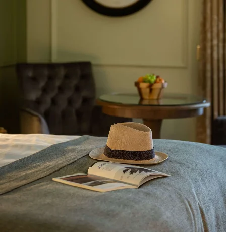 Elegant hotel room with decor, a cosy chair, and a hat on a bed.