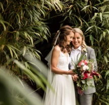 Couple embracing amid lush greenery at Fernhill House, holding a vibrant bouquet.