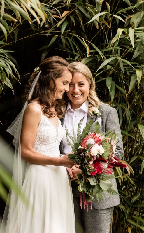 A happy couple smiles in a lush garden setting, surrounded by green foliage.