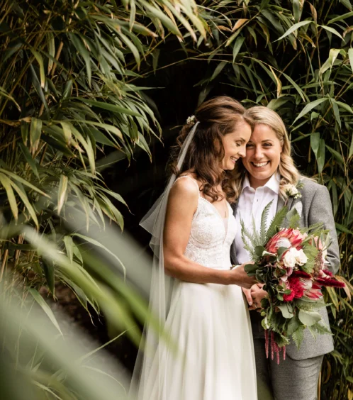 Couple embracing amid lush greenery at Fernhill House, holding a vibrant bouquet.