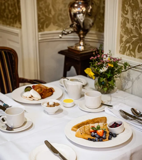 Elegant dining table with breakfast at Fernhill House Hotel, featuring fresh fruit and pancakes.