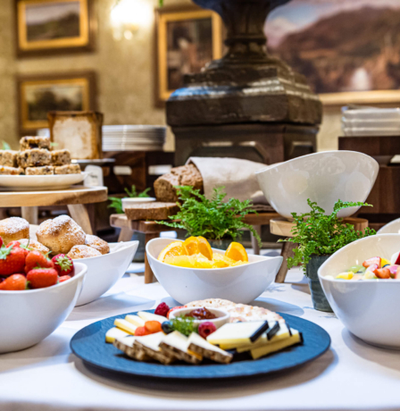 Elegant breakfast spread with fruits, pastries, and cheeses in a cosy hotel dining room.