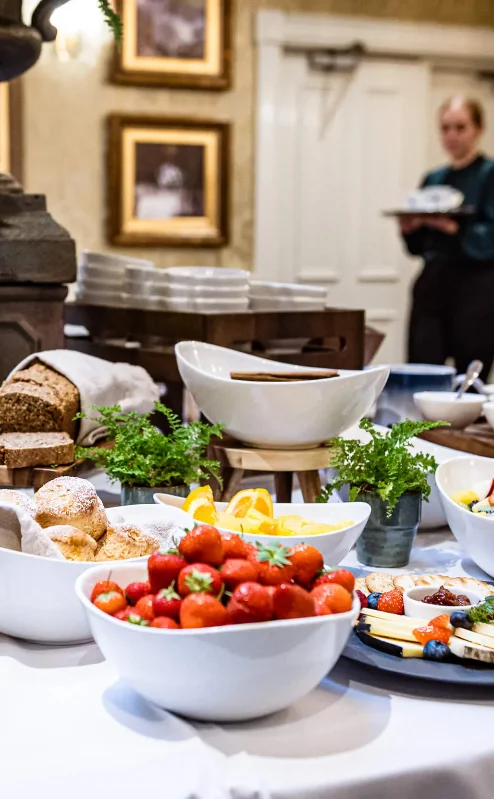 Elegant breakfast buffet with fresh fruit, pastries, and juices in a cosy dining room setting.