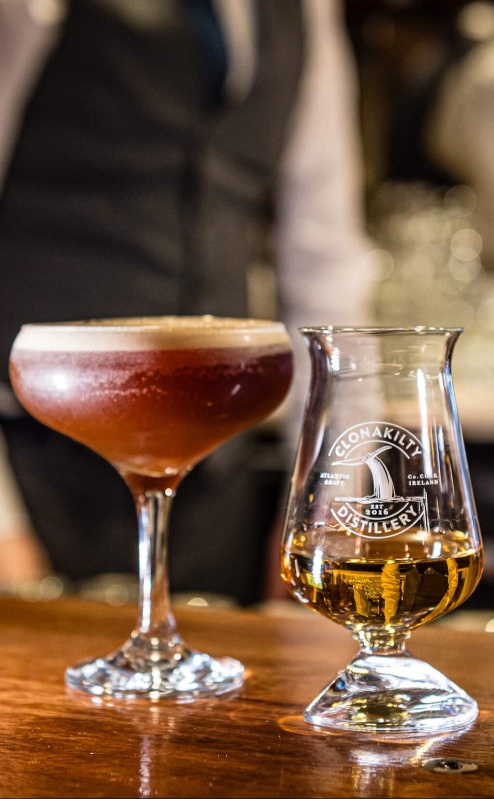 Cosy hotel bar with cocktails and whisky, bartender in background.