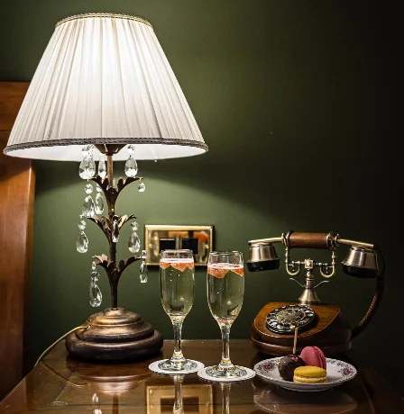 Elegant hotel room with lamp, vintage phone, champagne glasses, and macarons on a bedside table.
