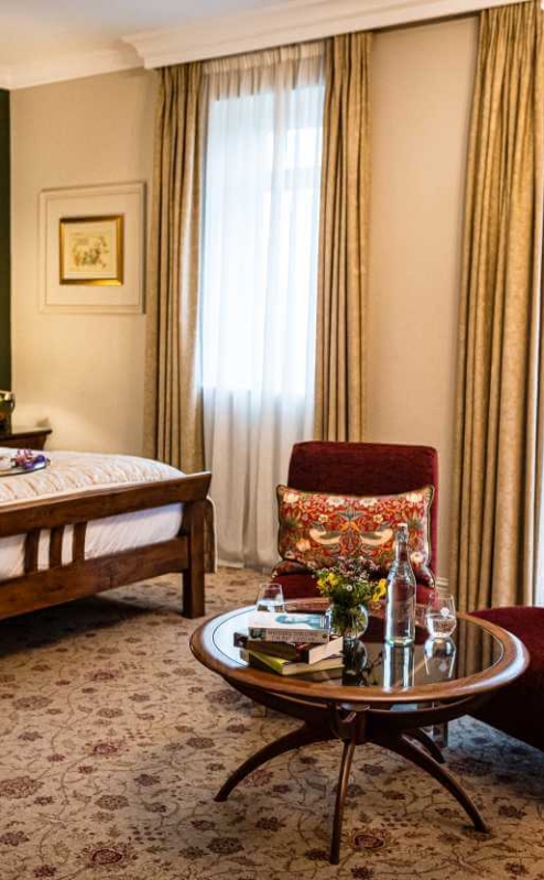 Elegant hotel room with double bed, cosy chairs, and warm natural lighting.