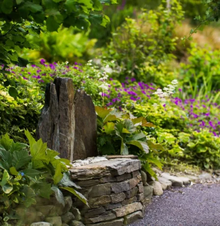 Lush garden path with colourful flowers and rustic stone seating.