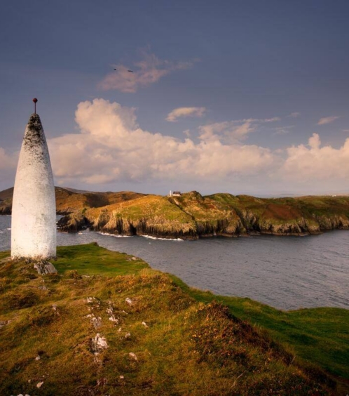 Scenic coastal view with lighthouse and rolling hills at sunset.