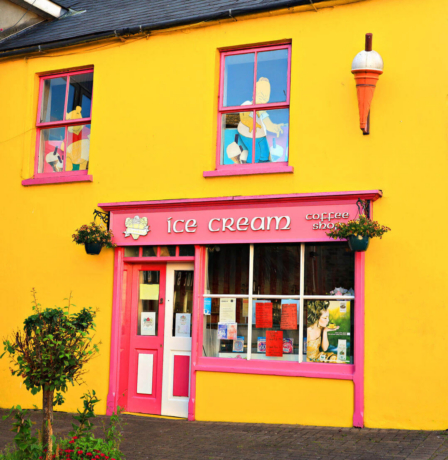 Vibrant yellow and pink ice cream shop exterior with hanging plants.