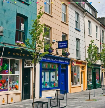 Colourful street with shops, hanging bunting, and families strolling in Fernhill House Hotel area.
