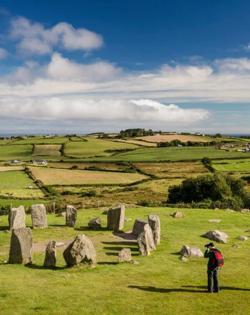 A couple exploring an ancient stone circle in a lush, green countryside under a blue sky.