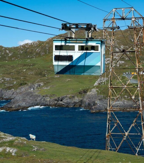 Cable car gliding over ocean with rugged hills in background on a clear day.