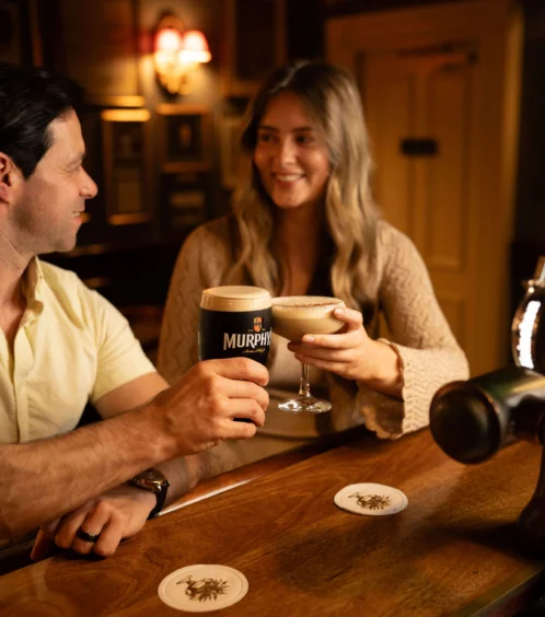 A couple enjoy drinks at a cosy Fernhill House Hotel bar, toasting with smiles.