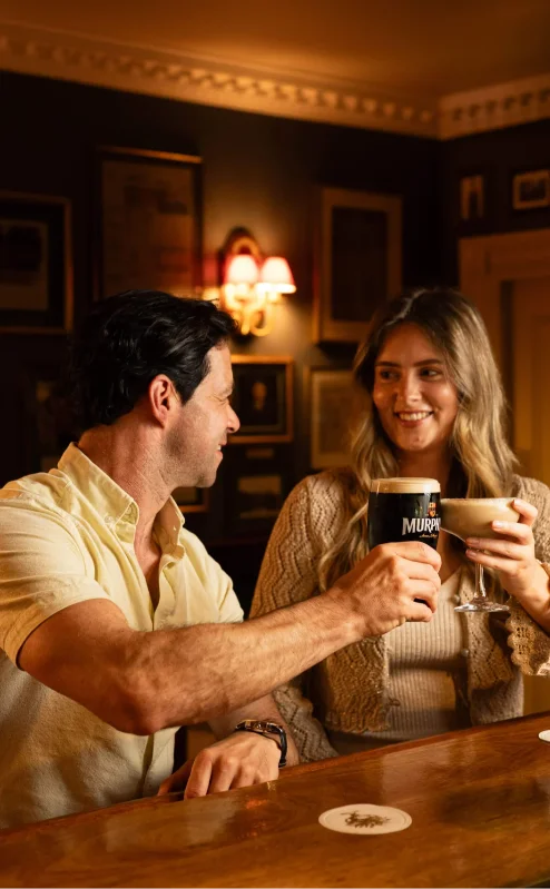 A couple enjoys drinks at a cosy, warmly-lit wooden bar inside Fernhill House Hotel.