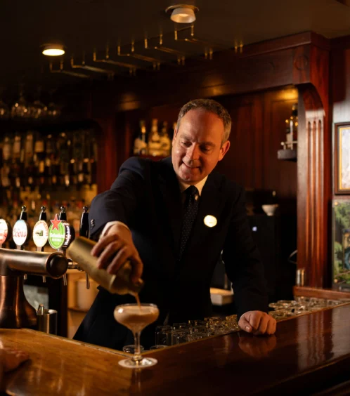 Bartender serving cocktails to guests in a cosy hotel bar setting.