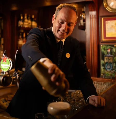 Bartender serving drinks in a cosy hotel bar setting with warm lighting.
