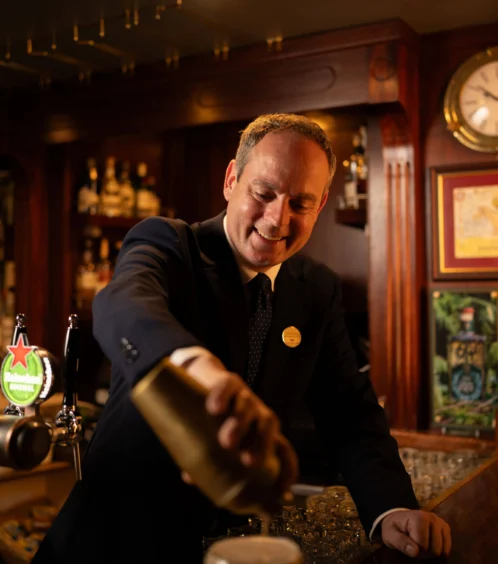 Bartender serving drinks in a cosy hotel bar setting with warm lighting.