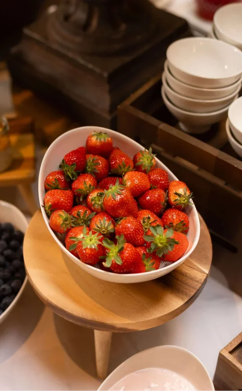 A hotel breakfast buffet with fresh strawberries, blueberries, cereals, and various bowls.