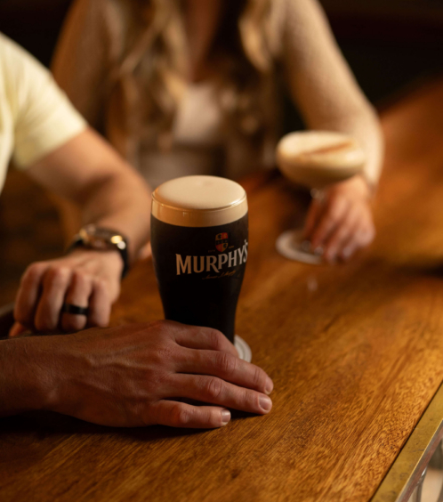 A couple enjoys drinks at a cosy bar, featuring a pint of Murphy's and a cocktail.