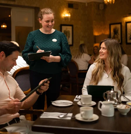 Friendly waiter serves a smiling couple at Fernhill House Hotel's cosy restaurant.