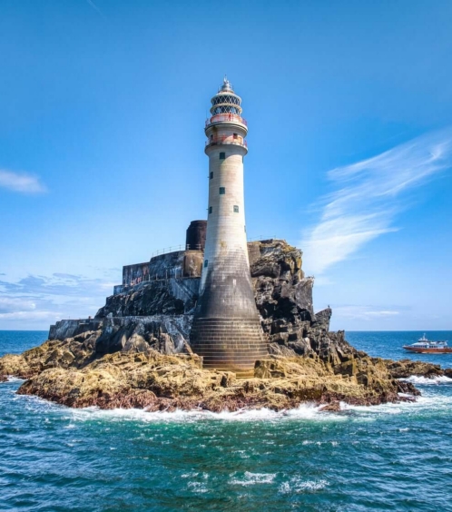 Scenic view of a lighthouse on a rocky island with a boat on the blue ocean.