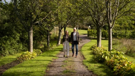 A couple strolls along a tree-lined path in a lush garden at Fernhill House Hotel.