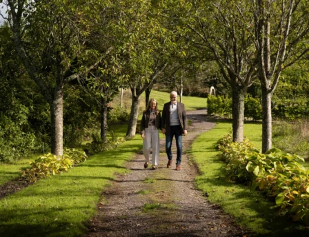 A couple strolls along a tree-lined path in a lush garden at Fernhill House Hotel.