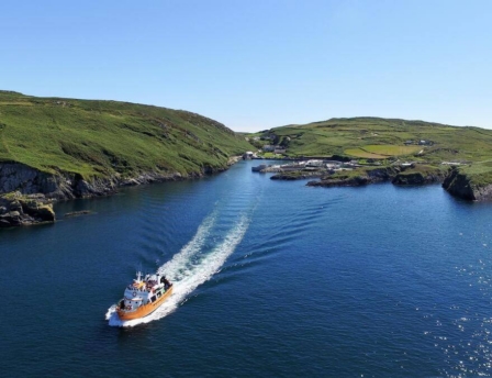 Scenic coastal view with a boat cruising through a calm bay under clear blue skies.