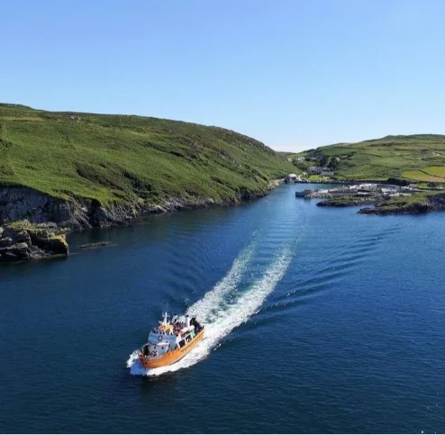 A boat sails through a serene, green landscape with cliffs and a clear blue sky.