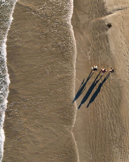 Aerial view of a family strolling along a sandy beach by the ocean waves.
