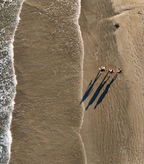 Aerial view of a family strolling along a sandy beach by the ocean waves.