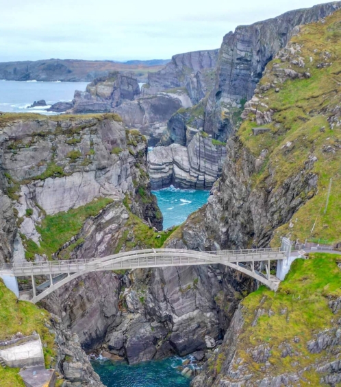 Family enjoying a scenic view from a bridge over a rocky coastal gorge.