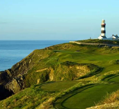 Coastal golf course with a lighthouse under a clear blue sky.