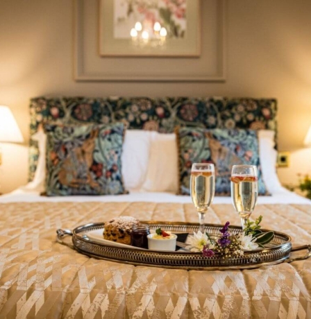 Cosy hotel room with a plush double bed, a welcome tray with desserts and champagne, soft lighting.