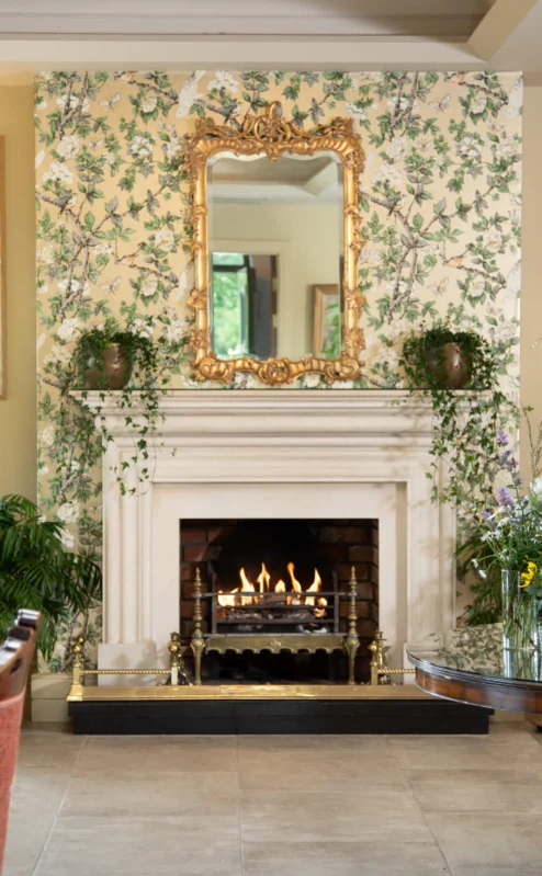 Cosy hotel lounge with fireplace, floral decor, and elegant seating.