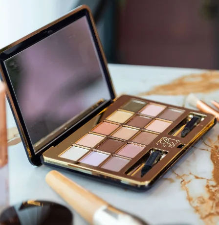 Makeup palette and brushes on marble table in hotel room.