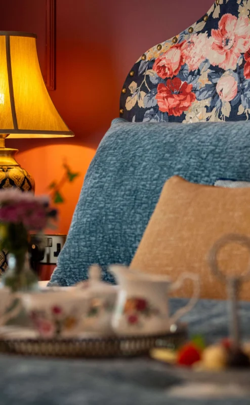 Cosy hotel room with floral decor, soft lighting, and a tea tray on the bed.