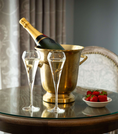 A champagne bottle in an ice bucket with two glasses and strawberries on a hotel table.