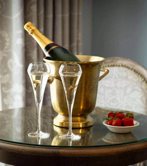 A table with champagne, flutes, and strawberries in a cosy hotel room.