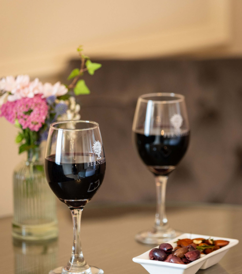 Two glasses of red wine and appetisers on a table in a cosy hotel lounge with flowers.