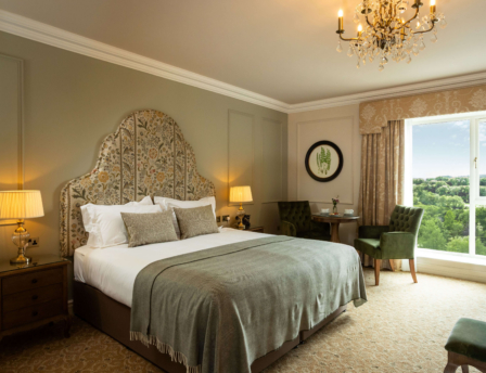 Elegant hotel room with large bed, sitting area, and scenic view from window.