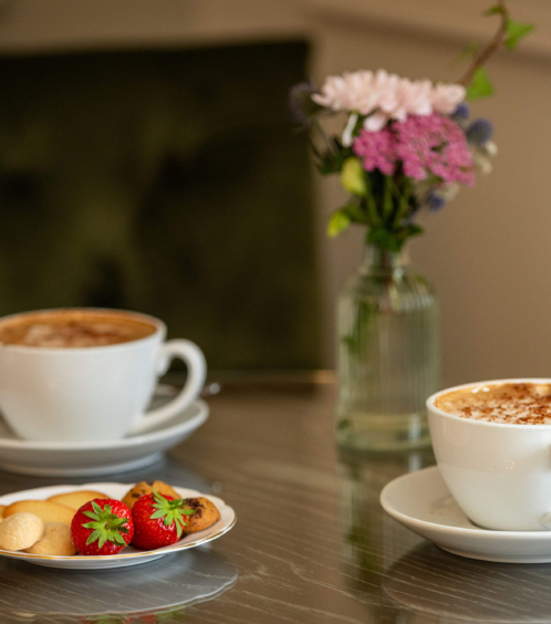 Two cups of coffee with biscuits and strawberries on a table in a cosy setting.