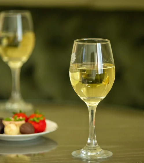 Two glasses of white wine and a plate of chocolates and strawberries on a glass table.